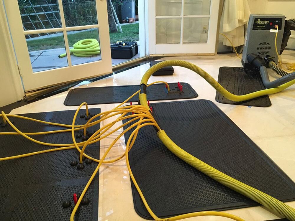 Hardwood floor drying mat system pulling water from beneath floorboards through hoses