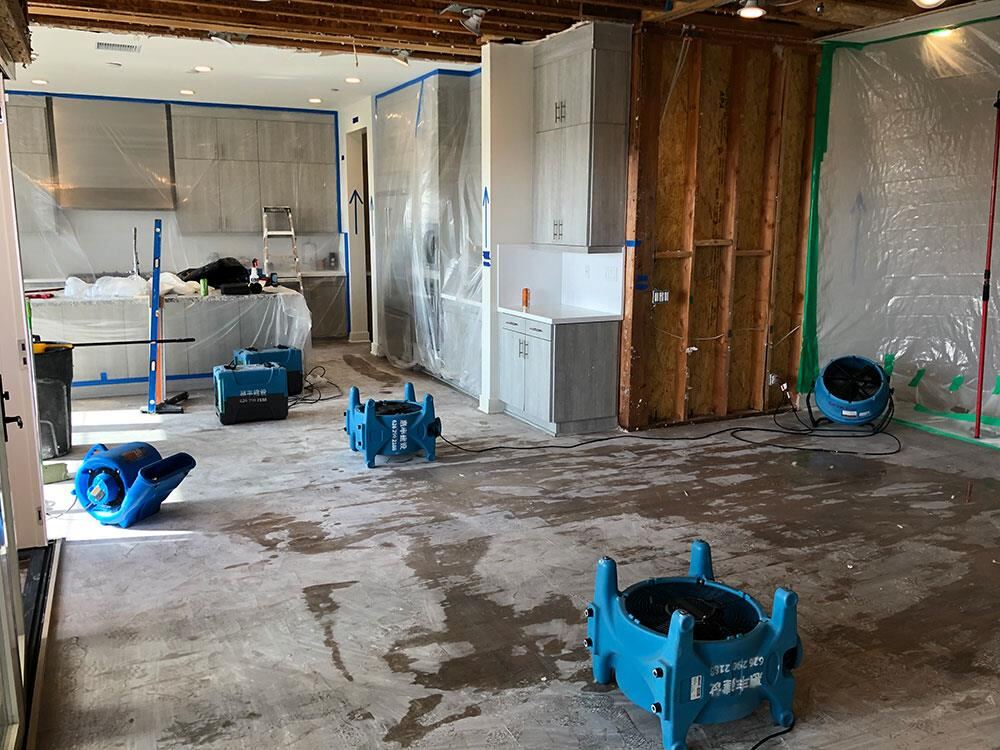 Extensively damaged kitchen with flooring and drywall removed inside plastic containment