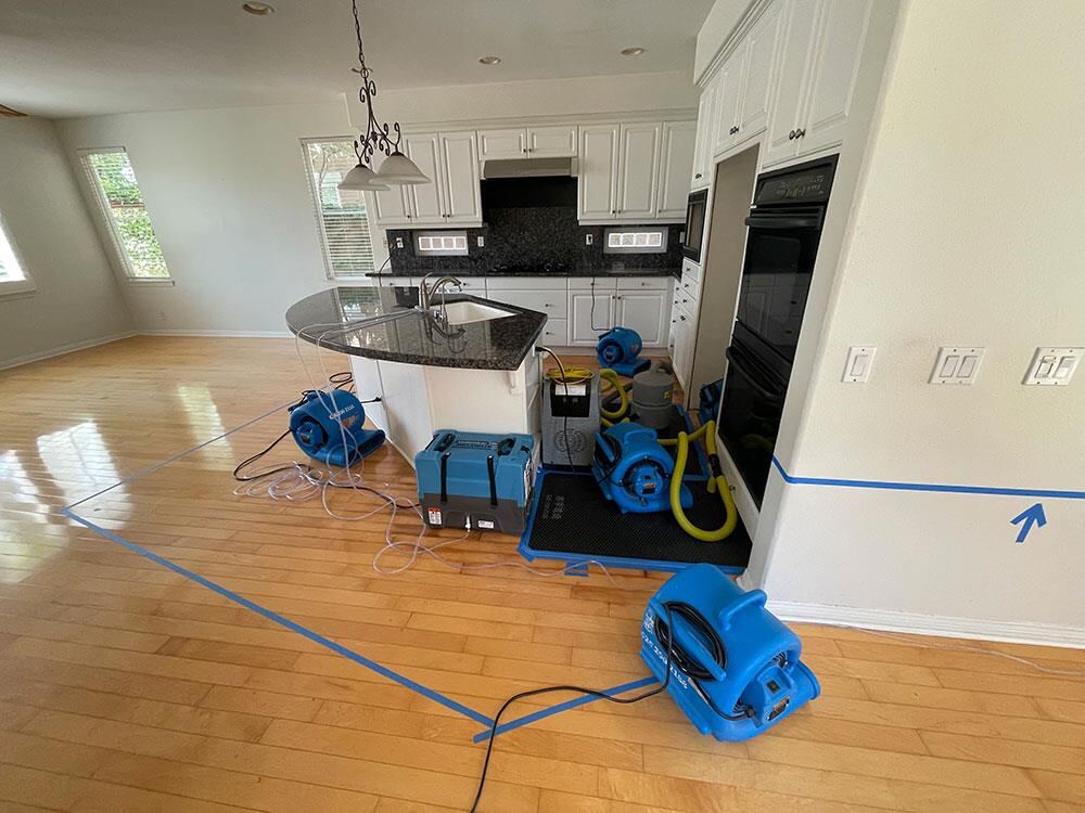 Open kitchen with air movers and dehumidifier drying hardwood around an island after a leak