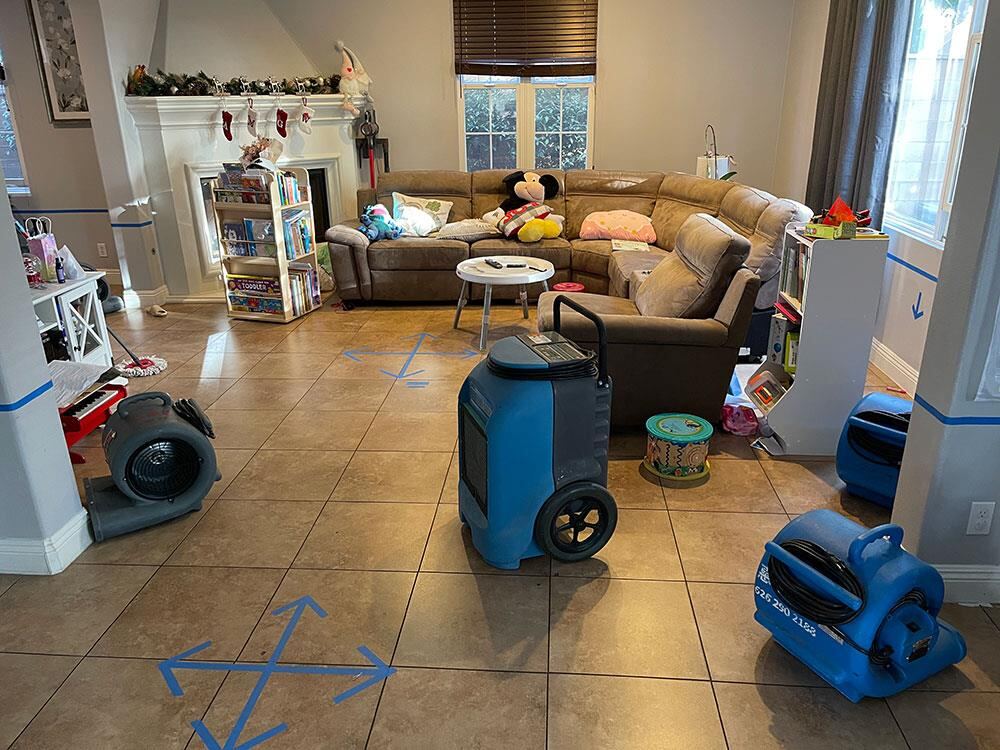 Industrial dehumidifier and air movers set up on a tile living room floor after a leak